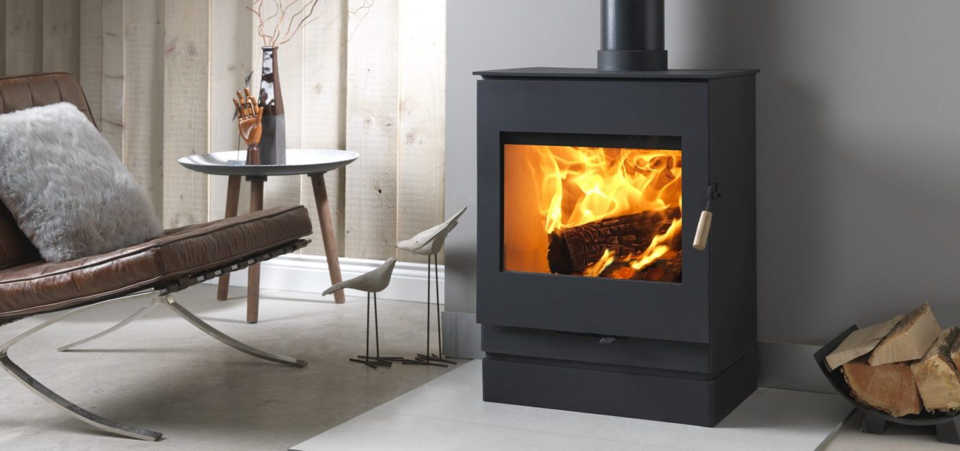 Black Square wood burning stove on a white hearth with leather chair to the left and log basket to the right